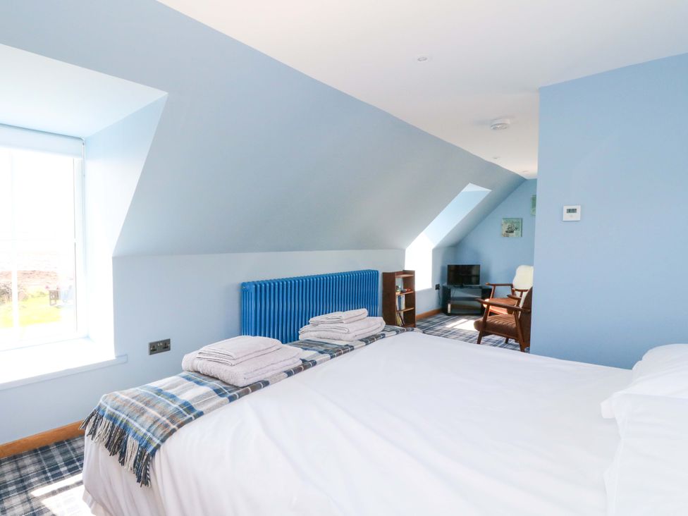 A bedroom with a bed, towels, bookshelf and chair at Post Cottage in Arisaig