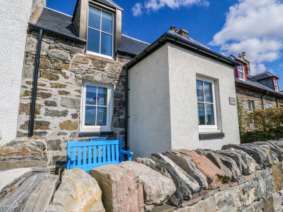 A building exterior with a blue bench and stone wall at Post Cottage in Arisaig