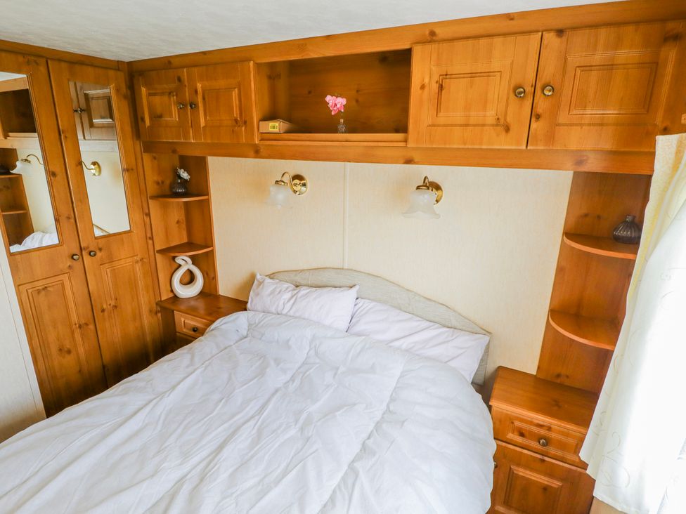 A bedroom with a bed, wood furniture, and shelves at Caravan 25 in Skegness