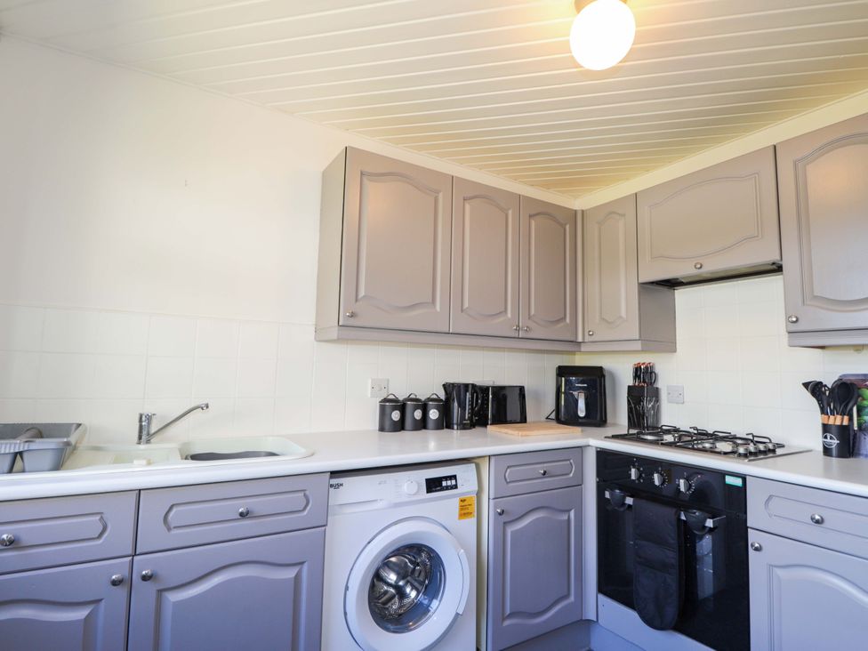 A kitchen with cabinets, sink, washing machine, and gas stove at 4A Carny Street Macduff