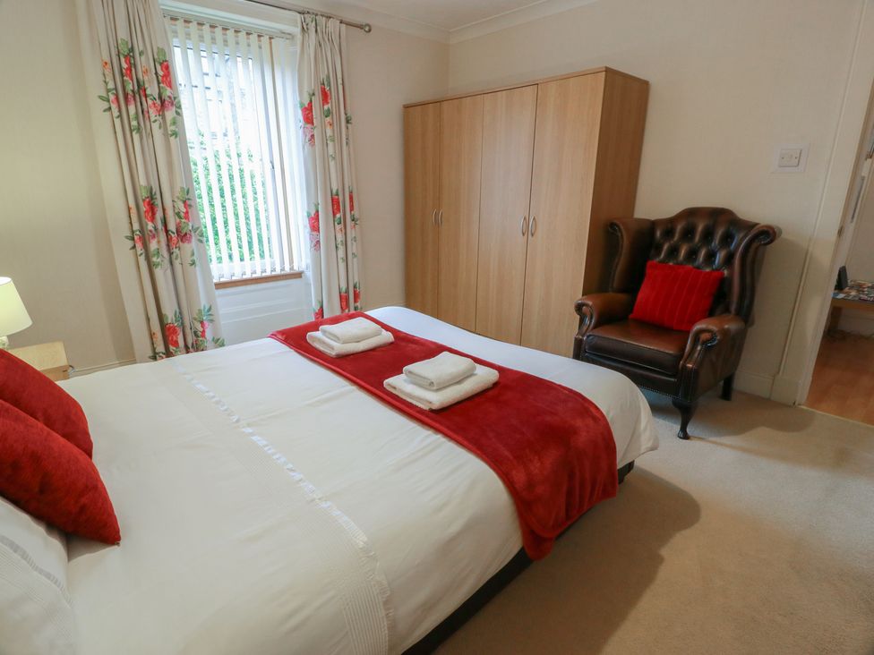A bedroom with a bed, wardrobe, and armchair at 2 St. Catherines Cottages in Perth