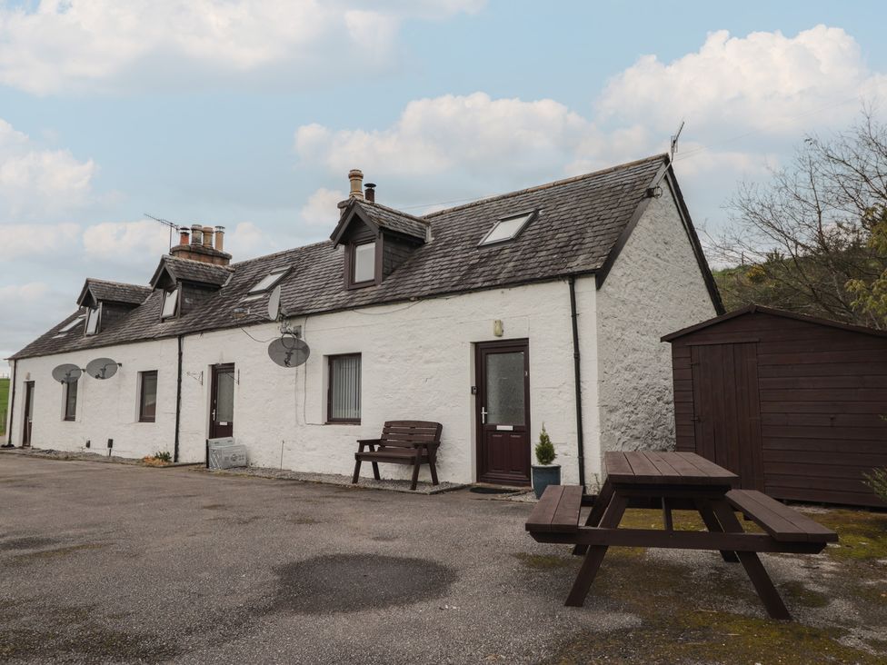 An outdoor area with a house, bench, and table at 3 Bruaich Cottages near Strathpeffer