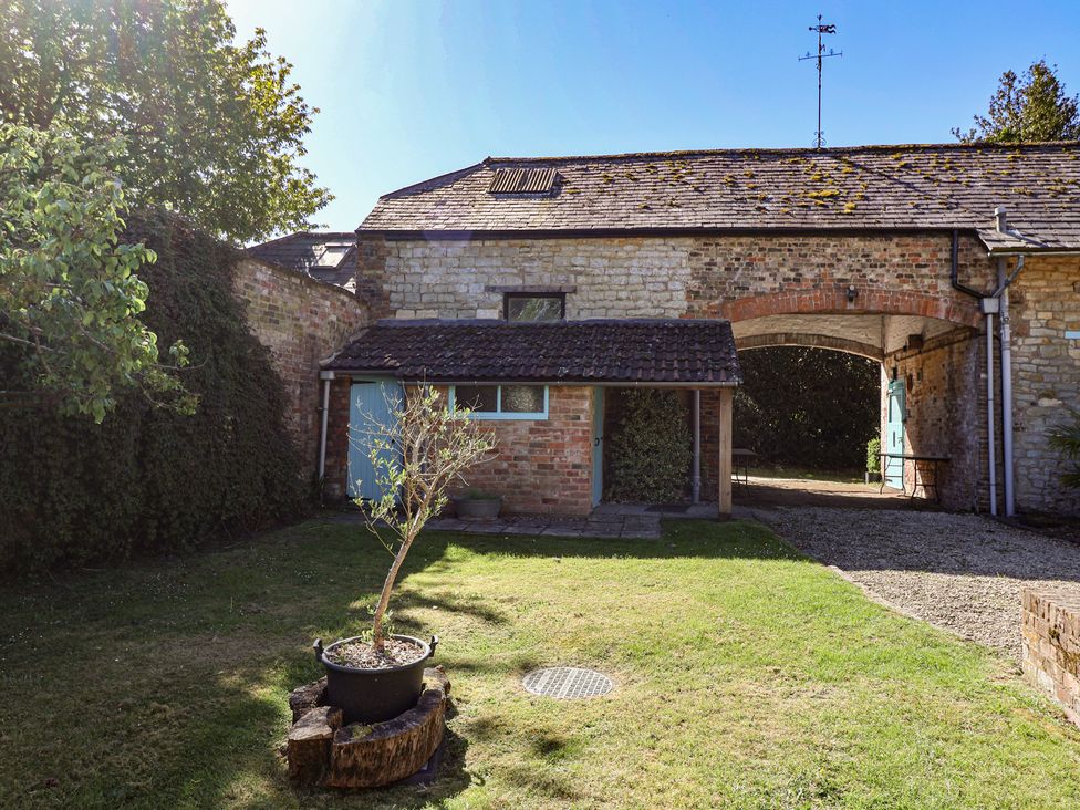 A garden with a building and archway at Harness Rooms in Gloucester