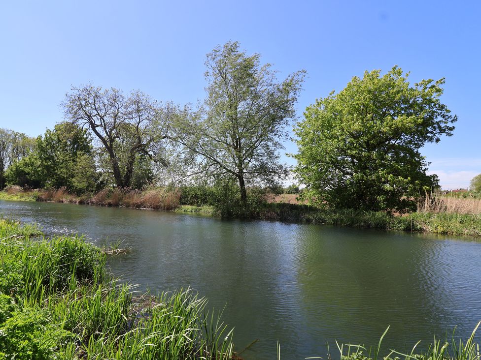 A river with trees and grass along the banks at Walk Farm Cottage in Gloucester