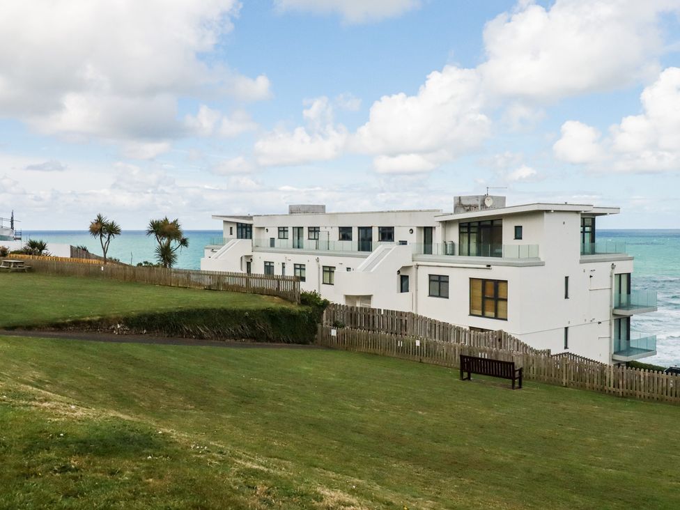A building near the ocean with grass and a bench at A5 Bay Apt.