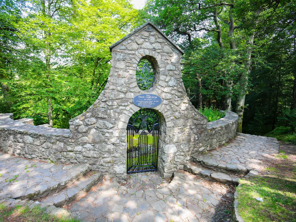 A stone structure with a gate and plaque surrounded by trees at Lodge 4 - Bron Eifion Criccieth