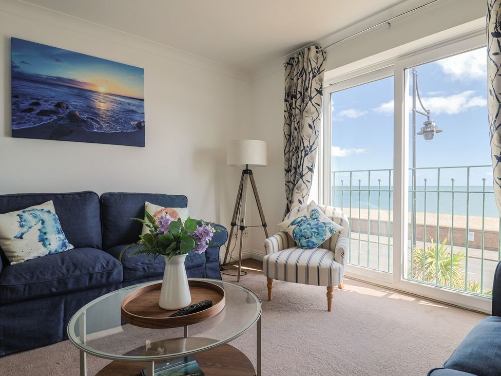 A living room with a sofa, table, and view of the sea at 2 Lyme Mews Seaton
