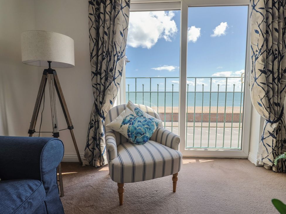 A living room with a chair and sliding door to the sea view at 2 Lyme Mews Seaton