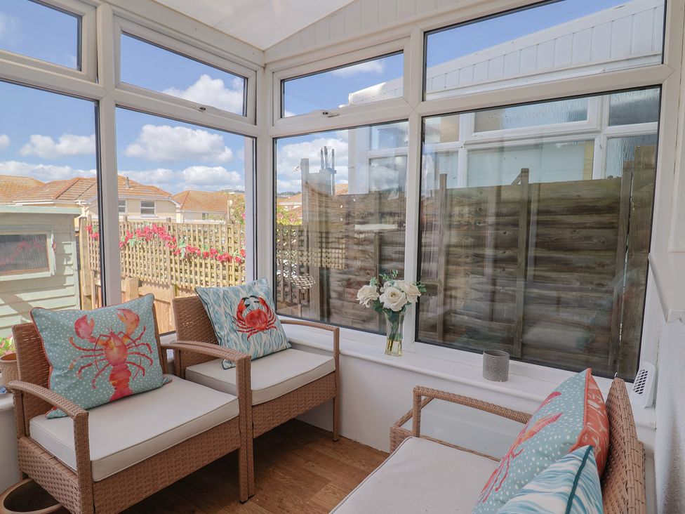 A conservatory with rattan chairs and flowers at 2 Lyme Mews Seaton
