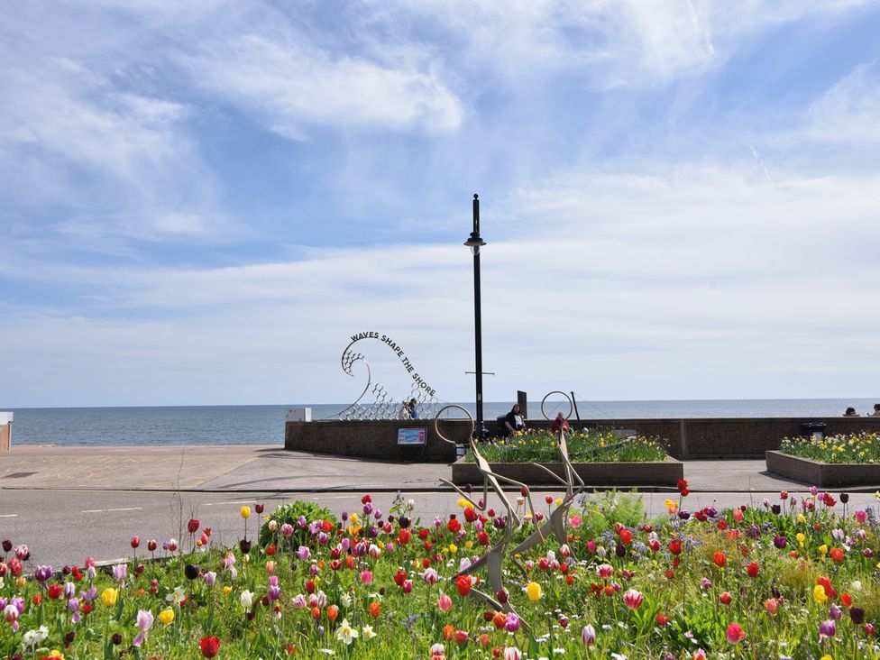 A view of flowers and a sculpture near the sea at 2 Lyme Mews Seaton