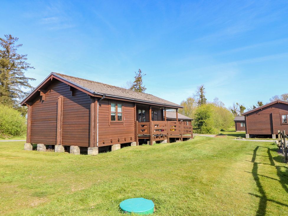 A brown wooden cabin with a deck in a grassy area at Lodge 8 - Sleep 4 - Double and Twin, Criccieth