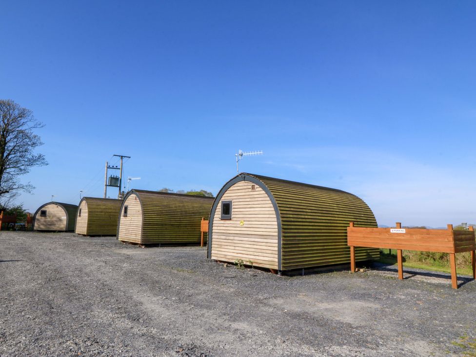 A row of wooden pods in a gravel area at Bron Eifion Pod 2 Criccieth