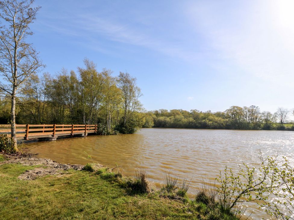 A lake with a wooden bridge and trees in the background at Bron Eifion Pod 2 Criccieth