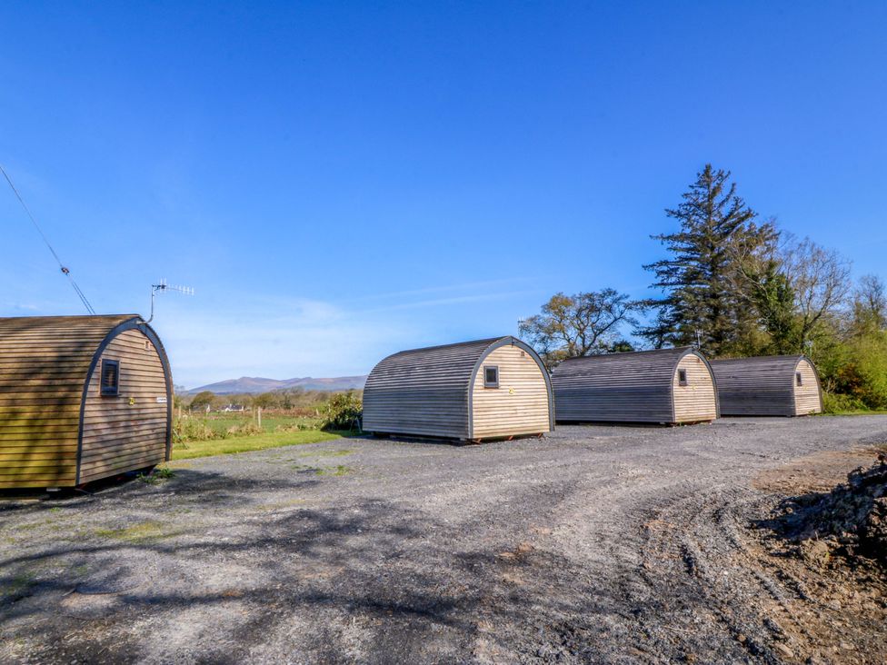 Four pods set on gravel with trees and mountains in the background at Bron Eifion Pod 3 Criccieth