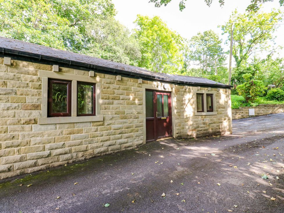 A stone building with windows and a door surrounded by trees at The Lodge in Brighouse