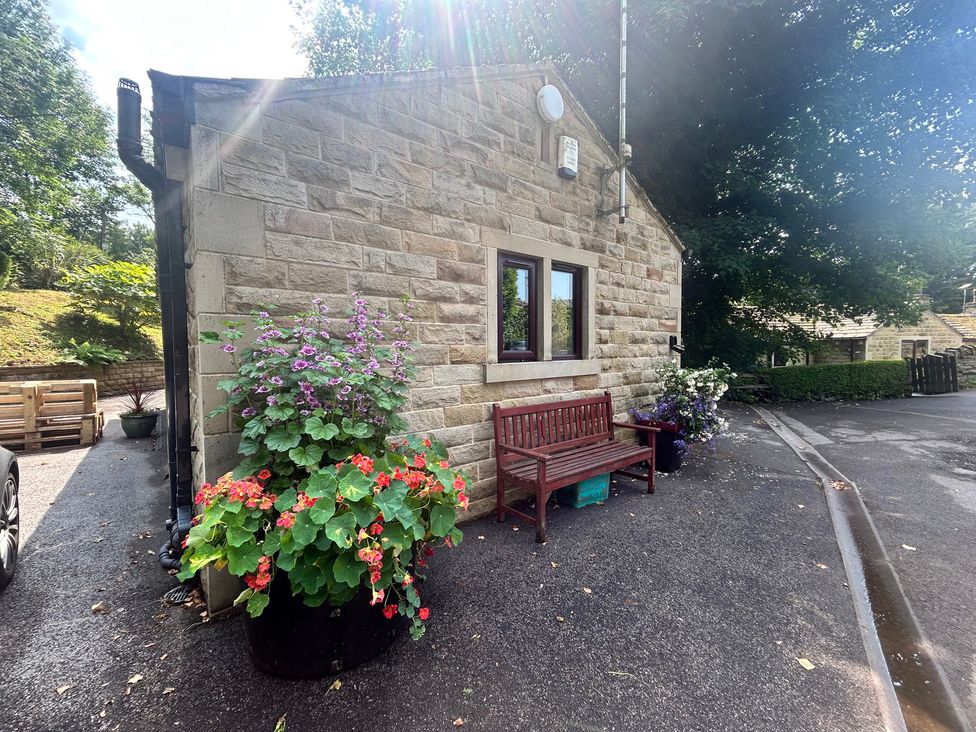 An outdoor area with a stone wall, wooden bench, and flower pots at The Lodge in Brighouse