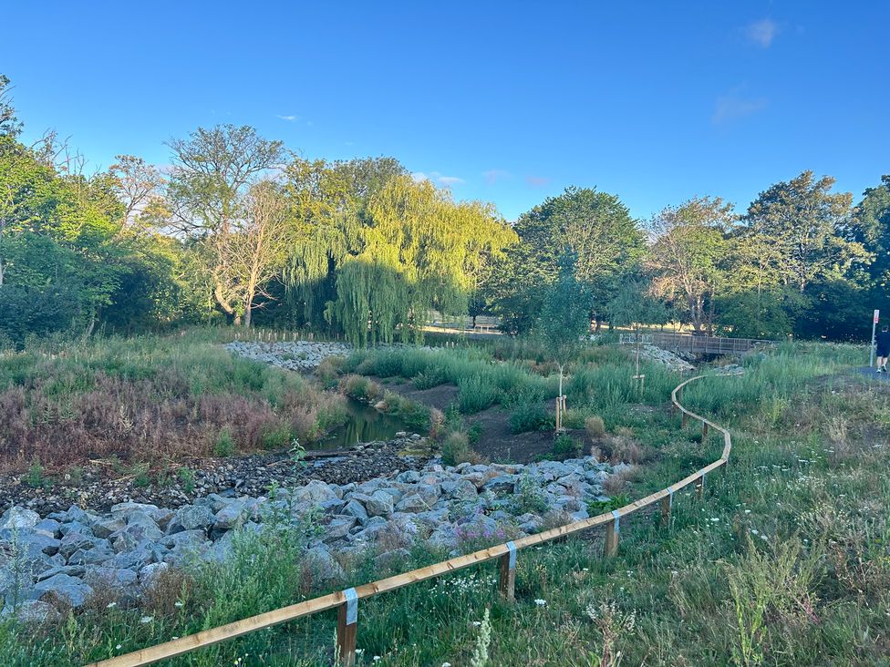A park with a stream, rocks, and greenery at The Lodge in Brighouse
