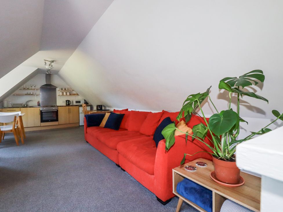 A living room with a red sofa and kitchen area at Camelia Cottage in St. Austell