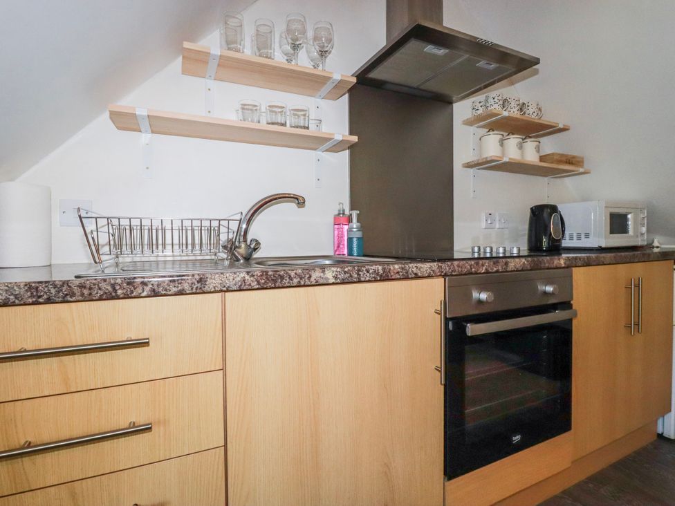 A kitchen with sink, oven, and shelves at Camelia Cottage St. Austell