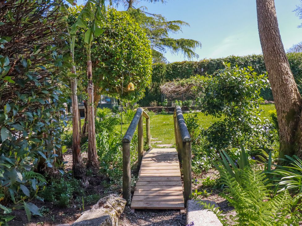 A garden with a wooden bridge and flowering plants at Camelia Cottage in St. Austell