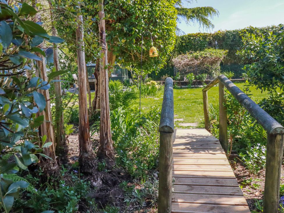 A garden with a wooden bridge and trees at Camelia Cottage in St. Austell