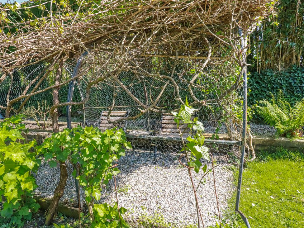 A swing seat surrounded by plants and gravel at Camelia Cottage in St. Austell