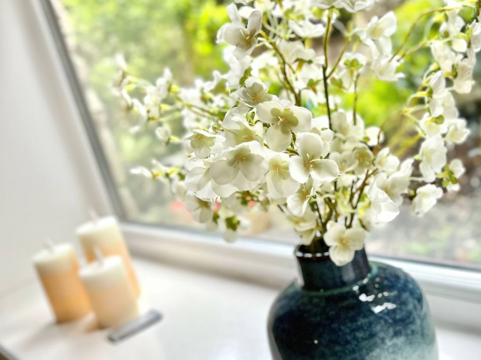 A vase with flowers and candles on a windowsill at Hydrangea Cottage in Tregrehan Mills near St. Austell