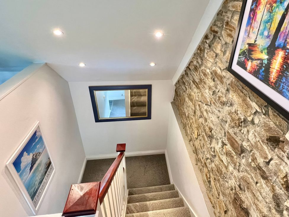 A staircase with a mirror and stone wall at Hydrangea Cottage in Tregrehan Mills near St. Austell