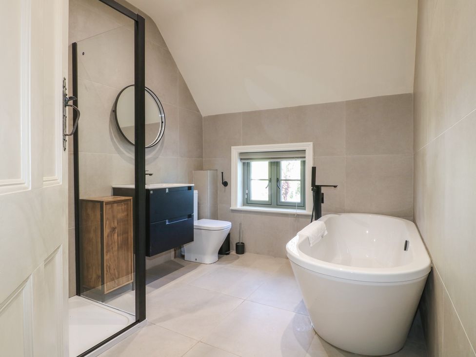 A bathroom with a bathtub, toilet, sink, and mirror at Gardener’s Cottage in Oakham