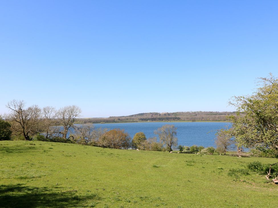 A view of a lake surrounded by grass and trees at Gardener’s Cottage in Oakham
