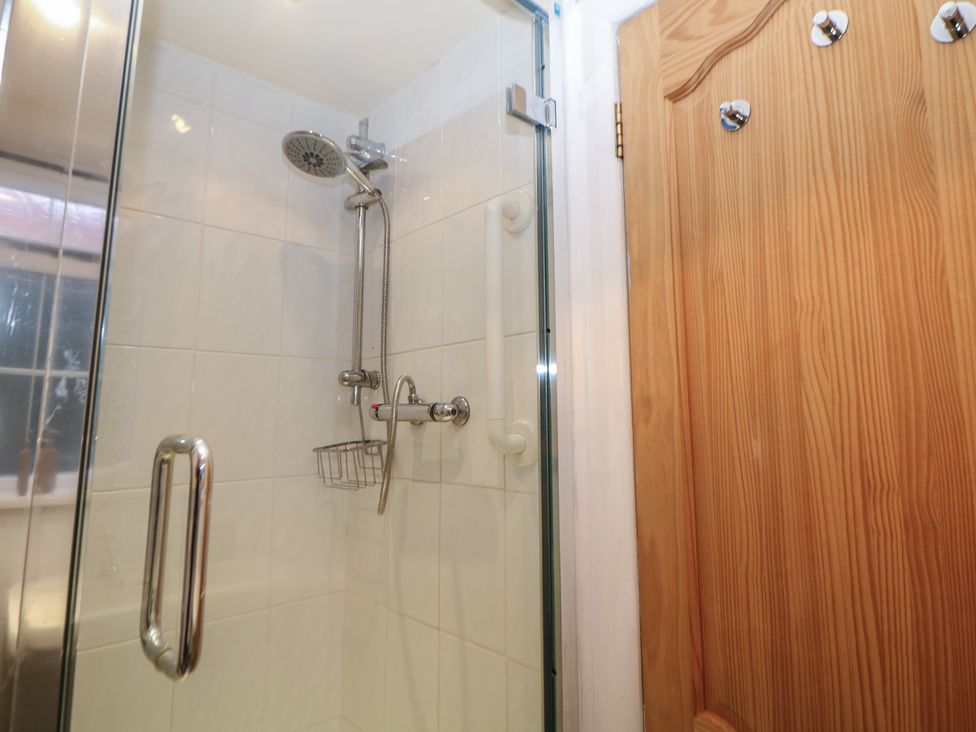 A bathroom with a shower and a wooden door at Ivy Cottage in Matlock