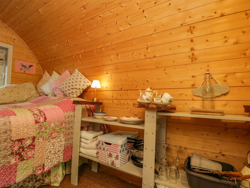 A bedroom with a bed and shelf containing dishes at Bluebell Glamping Pod in Woolton Hill