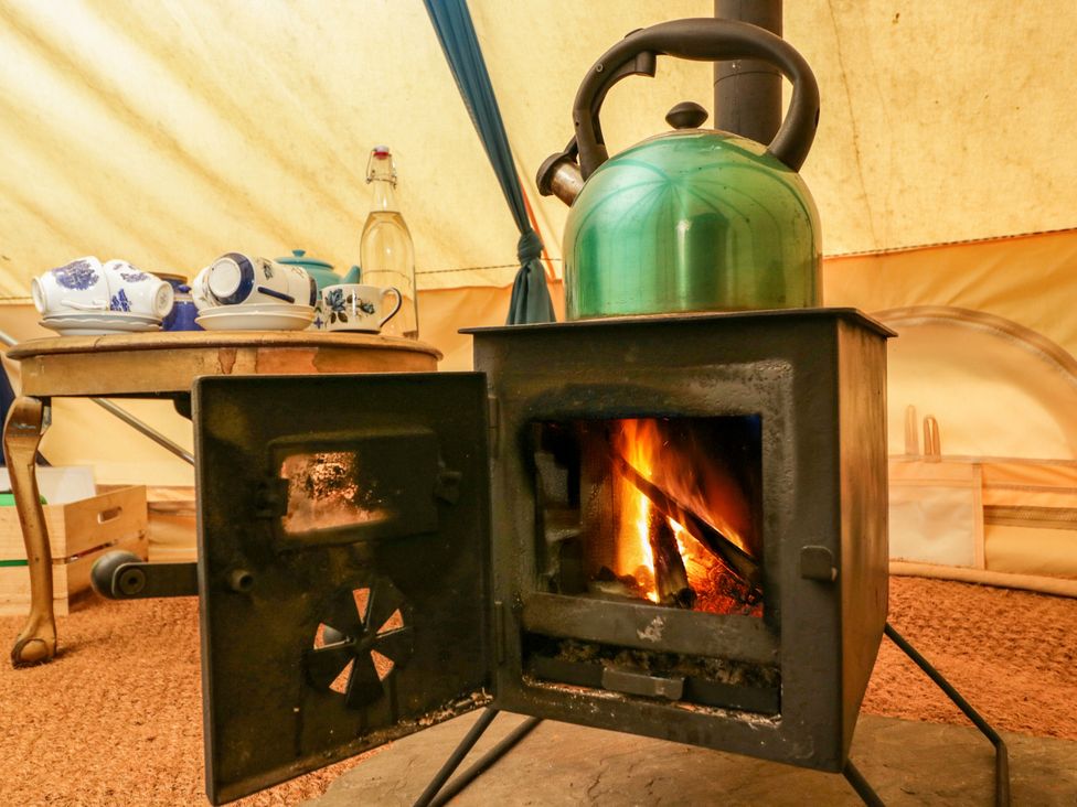 A stove with a kettle on top and a table with dishes at The Moroccan Bell Tent in Woolton Hill