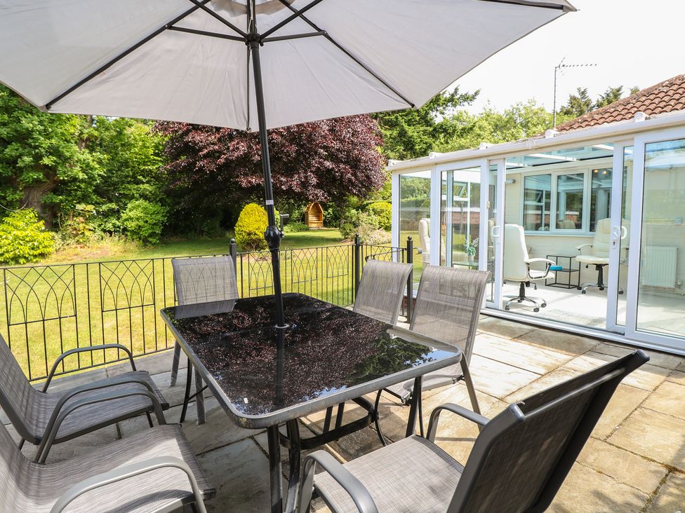 A garden with a table and chairs under an umbrella near a glass conservatory at 51 Colin McLean Road Dereham