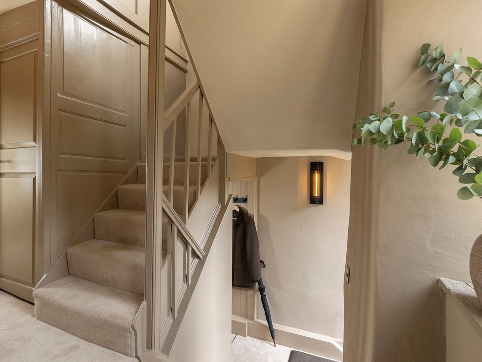 A staircase with a coat and umbrella in a hallway at Church Alley House Stow-On-The-Wold
