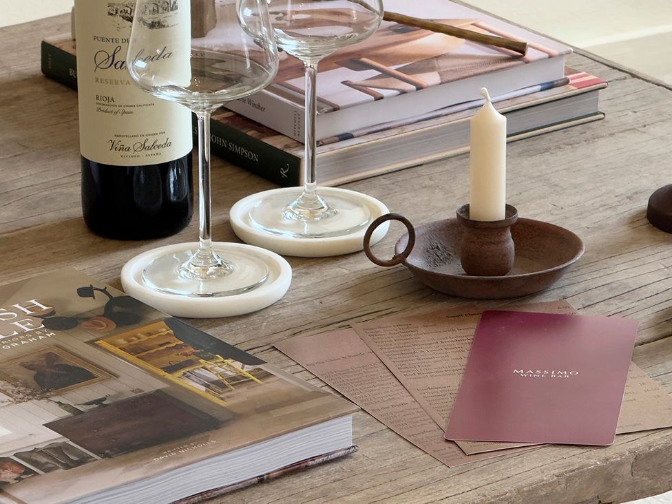A living room table with wine glasses, a wine bottle, candle, and books at Church Alley House Stow-On-The-Wold