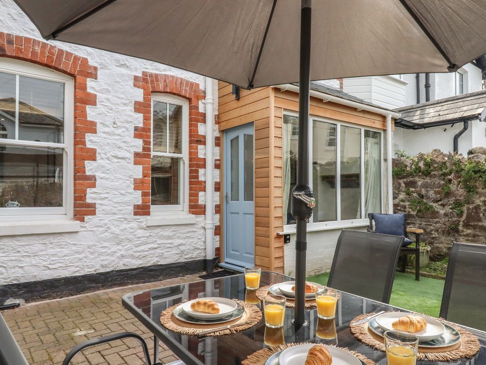 A patio with a table and chairs under an umbrella at Hares Cottage in Torquay