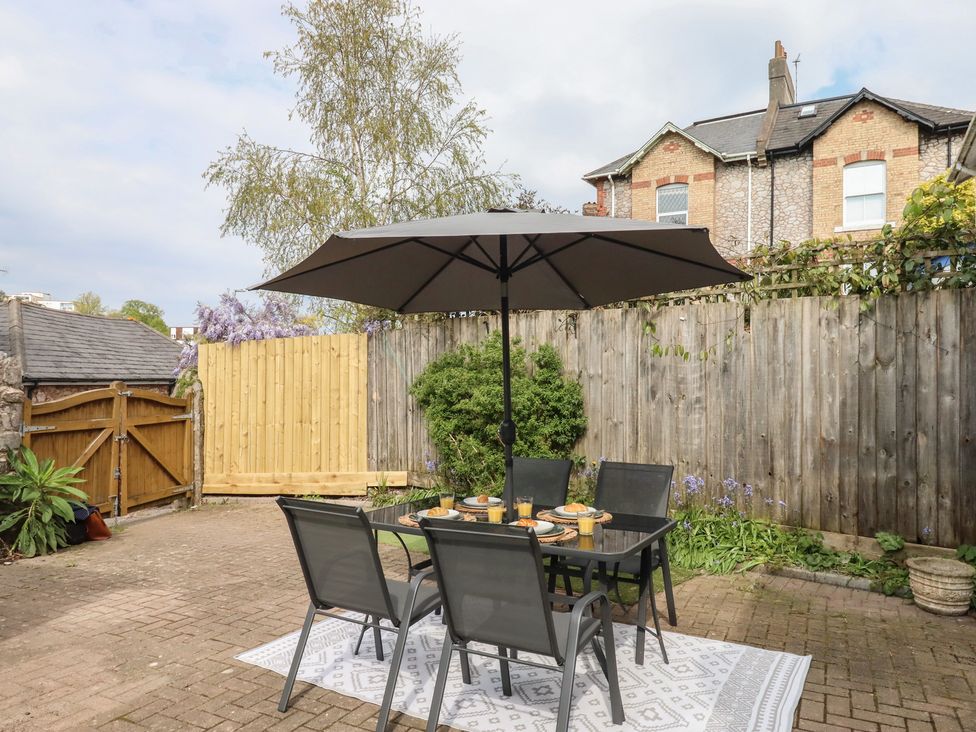 A garden with a dining table and chairs under an umbrella at Hares Cottage in Torquay
