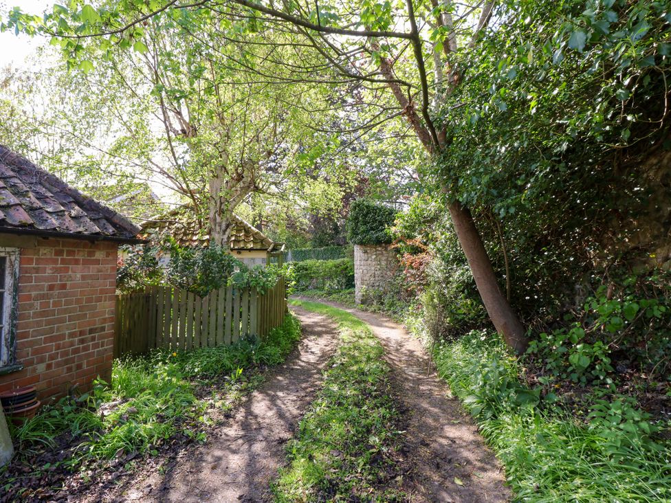 A garden pathway surrounded by trees and a brick building at The Cook’s Cottage in Malton