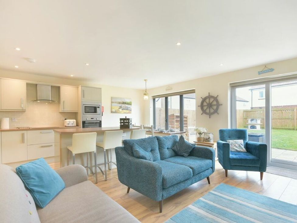 A living room with a sofa and kitchen area at Beach Walk in Chathill
