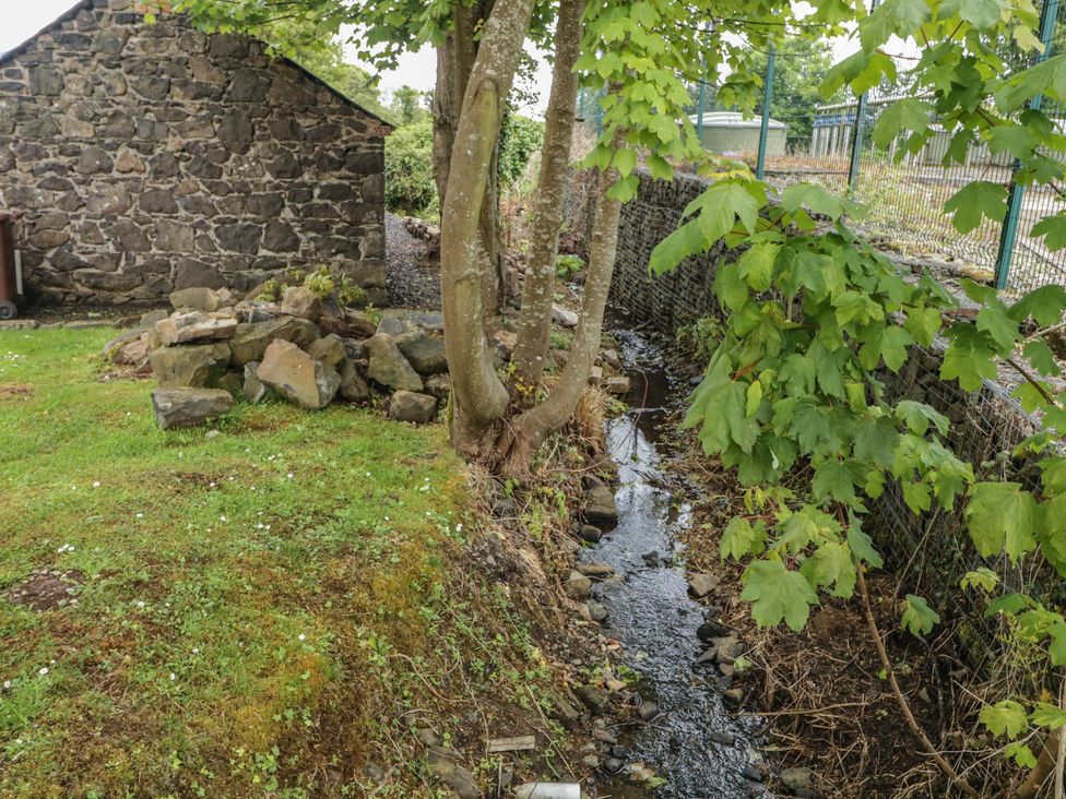 An outdoor area with a stone wall, trees, and a stream at Brook Cottage in Coleraine