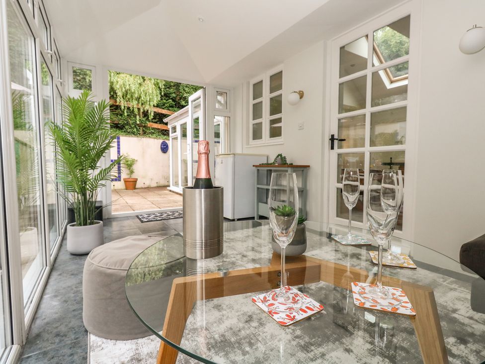 A conservatory with a table and wine glasses at Woodbine Cottage in Weymouth