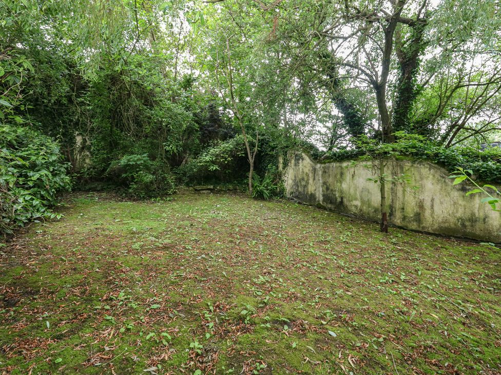 A garden with trees and a wall at Woodbine Cottage in Weymouth