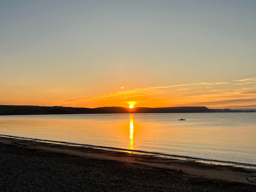 A sunset over water with a boat in the distance at Woodbine Cottage in Osmington
