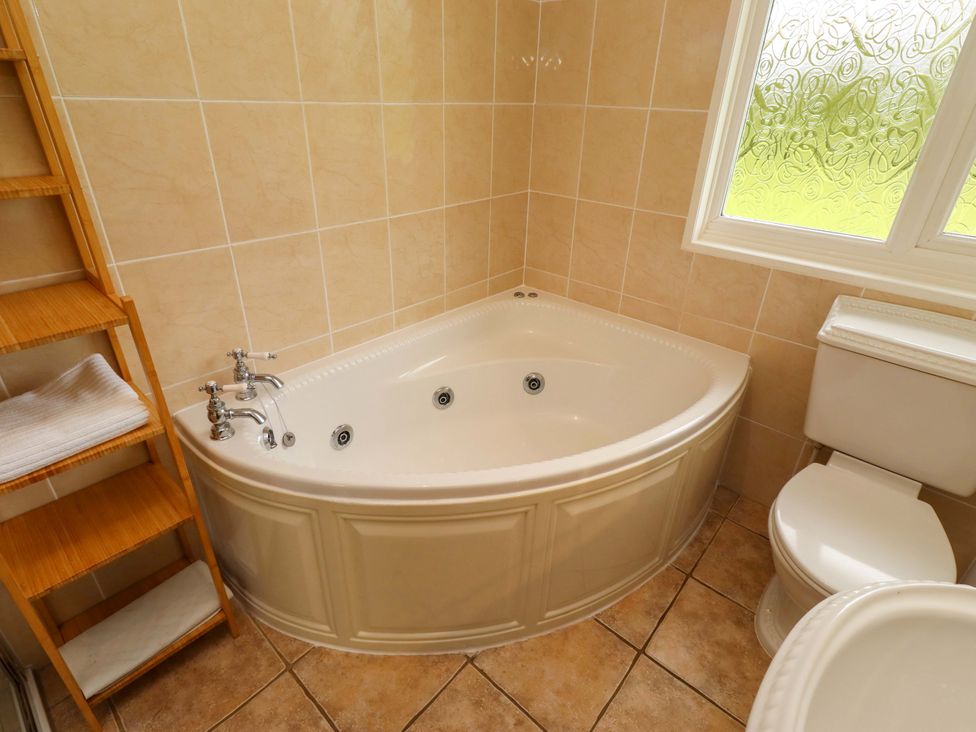 A bathroom with a bathtub, toilet and shelves at Campden in Rennington near Embleton