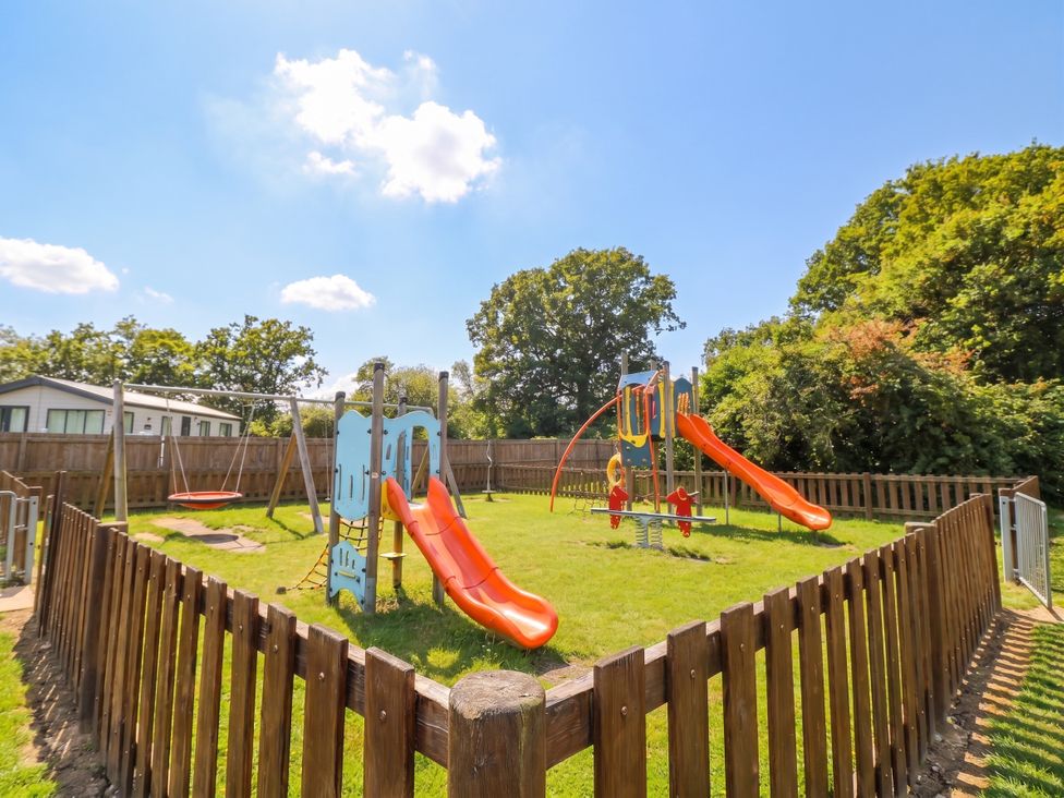 A playground with slides swings and grass at Forest Retreat - FO26 Saxmundham
