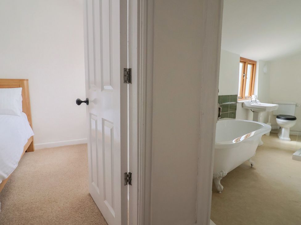 A bedroom with a bed and a door leading to a bathroom at Saybrook Cottage Charmouth