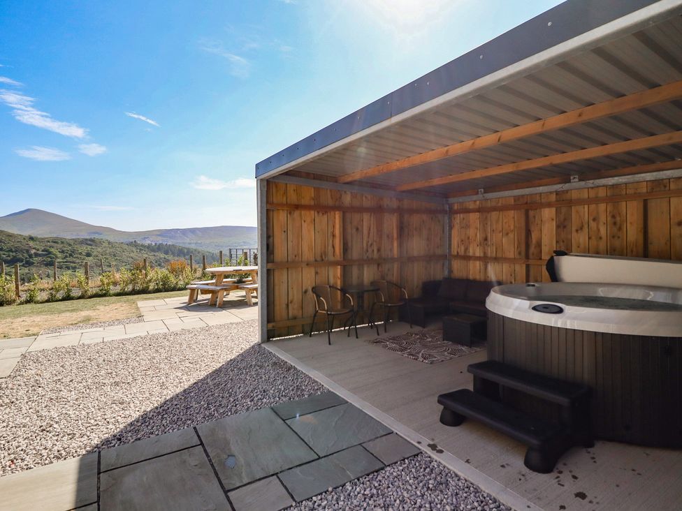 An outdoor patio with a hot tub and wooden furniture at Tyn Y Weirglodd in Deiniolen