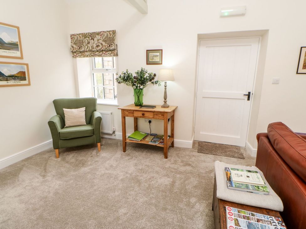 A living room with a green armchair and wooden table at Dairy Cottage in Kirkby Stephen