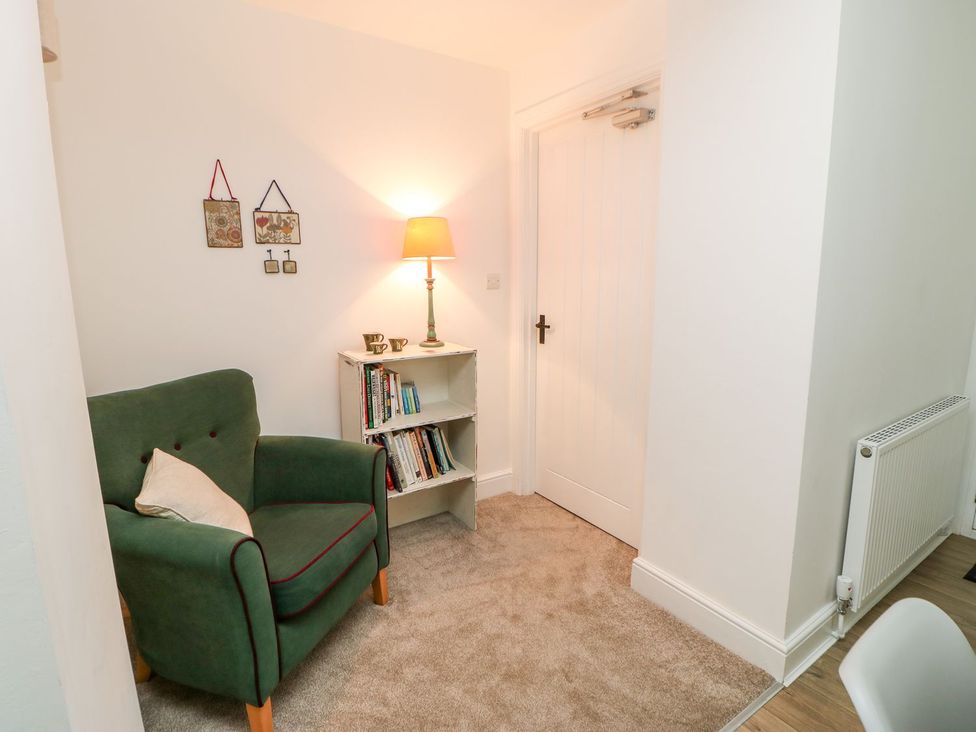 A sitting room with an armchair and bookshelf at Dairy Cottage in Kirkby Stephen